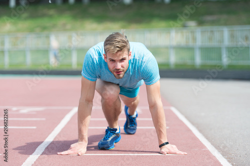 Man runner on start position at stadium. Runner in start pose on running surface. Man run outdoor at running track. Sport and athletics concept. Sportsman on concentrated face ready to go