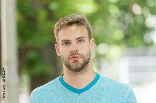 Man with bristle on calm face, nature background, defocused. Man with beard or unshaven guy looks handsome outdoor. Guy bearded and attractive cares about his appearance. Skin care concept