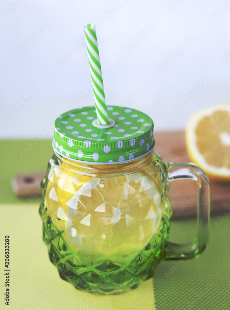 Lemonade with fresh lemon. Detox water for a healthy diet and cleansing the body. A beautiful glass mug with a lid and a drinking tube. Infused water with lemon. Stock Photo
