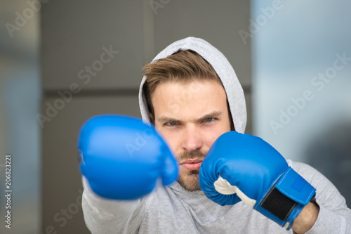 Boxing concept. Man athlete on concentrated face with sport gloves practicing boxing punch, urban background. Boxer with hood on head practices jab punch. Sportsman boxer training with boxing gloves photo