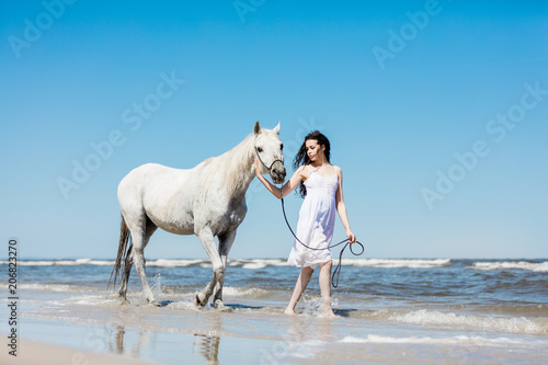 Girl walking on the beach with white horse.