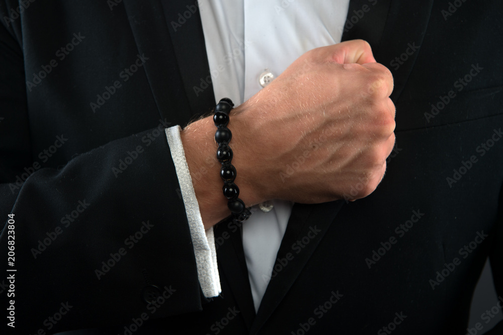 Male fist with bracelet on formal suit background. Bracelet or amulet on wrist. Amulet concept. Hand of business person with amulet made out of black beads. Symbol of luck or fashionable accessory