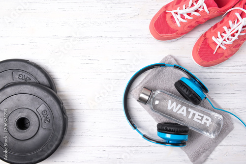 Fitness concept, pink sneakers, bottle of water, weight plates and blue headphones on wooden background, top view