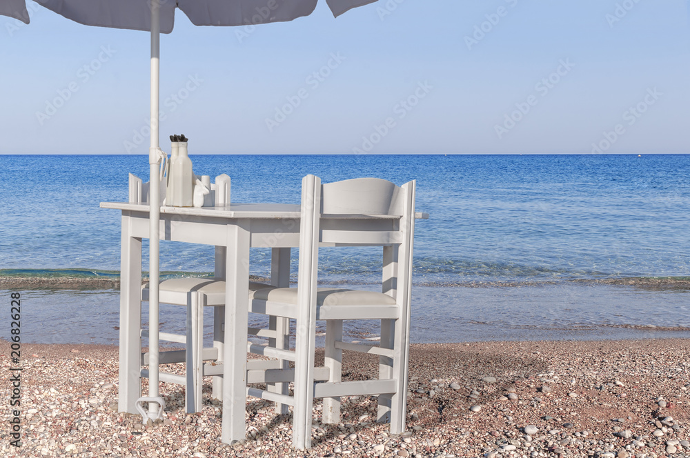 Fototapeta premium Two white chair and umbrella with wooden table on pebble beach