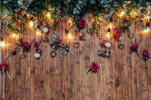 Fototapeta Naklejka Na Ścianę i Meble -  Rustic wedding photo zone. Hand made wedding decorations includes Photo Booth  red flowers. Garlands and light bulbs
