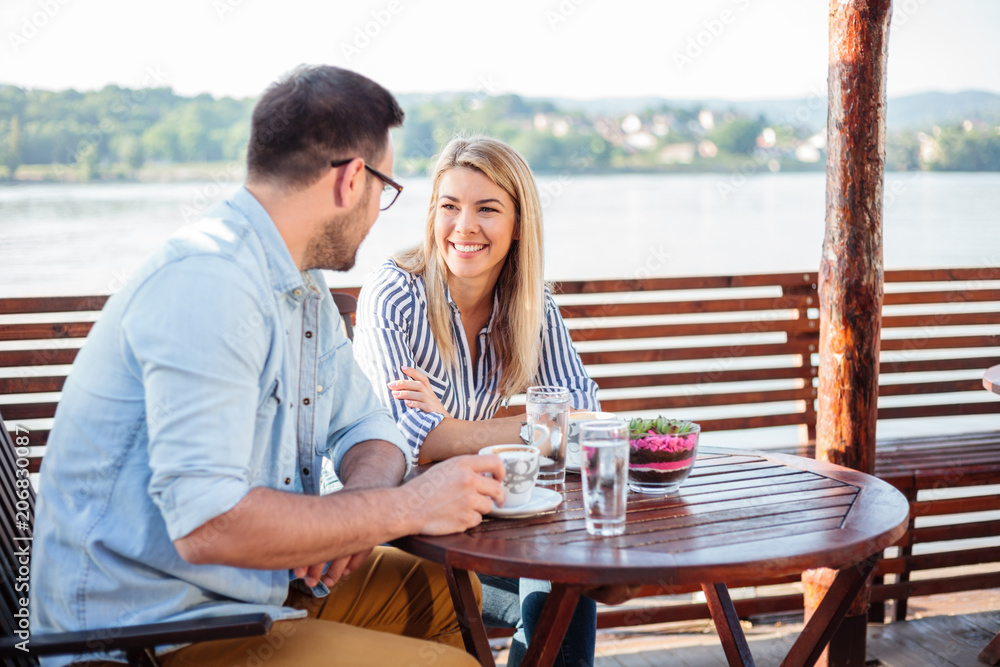 Young couple enjoying time in a riverside cafe. Drinking coffee and talking. Danube in background.