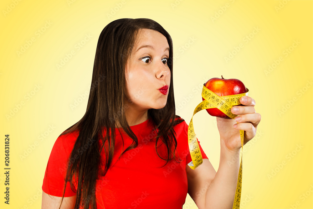 Portrait of young woman holds red apple coiled measuring tape, isolated on yellow background. Portrait of young woman holds red apple coiled measuring tape, isolated on yellow background.