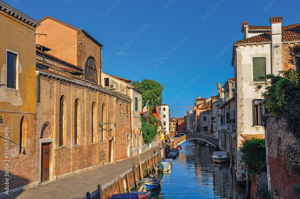 Naklejka premium Panoramic view of buildings, bridge and boats in front of a canal at the sunset, in the city center of Venice, the historic and amazing marine city. Located in the Veneto region, northern Italy