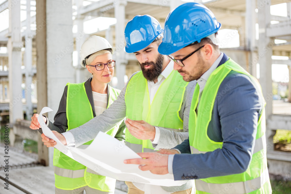 Mixed group of engineers or business partners at construction site, working together on building's blueprint. Architecture and teamwork concept. Mixed group of engineers or business partners at construction site, working together on building's blueprint. Architecture and teamwork concept.