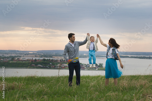 Parents hold their son s hands and raise  the baby jumps  cloudy