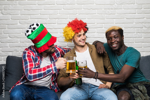 Three happy men sitting on couch and watching sport on TV and cheers beer photo