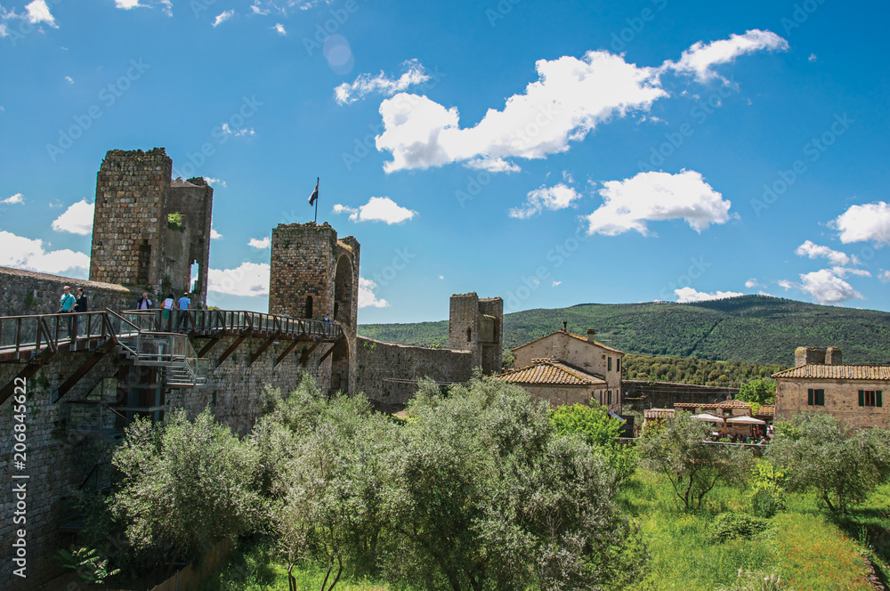 View of buildings and trees from above the walls of the Monteriggioni hamlet. A medieval fortress, surrounded by stone walls, at the top of a hill, near Siena. Located in the Tuscany region 