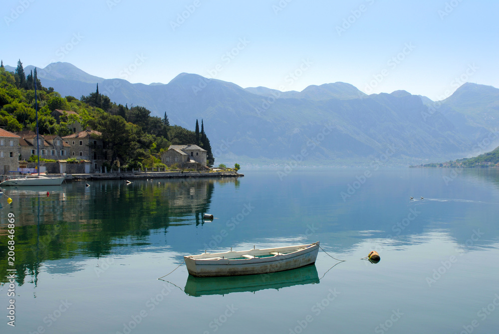 Boat on still water against mountain ridge and ancient city. Bay of Kotor, Montenegro