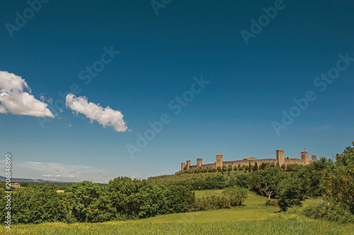 View of the stone walls of the hamlet of Monteriggioni on top of hill and surrounded by trees. A medieval fortress, surrounded by walls at the top of a hill near Siena. Located in the Tuscany region 