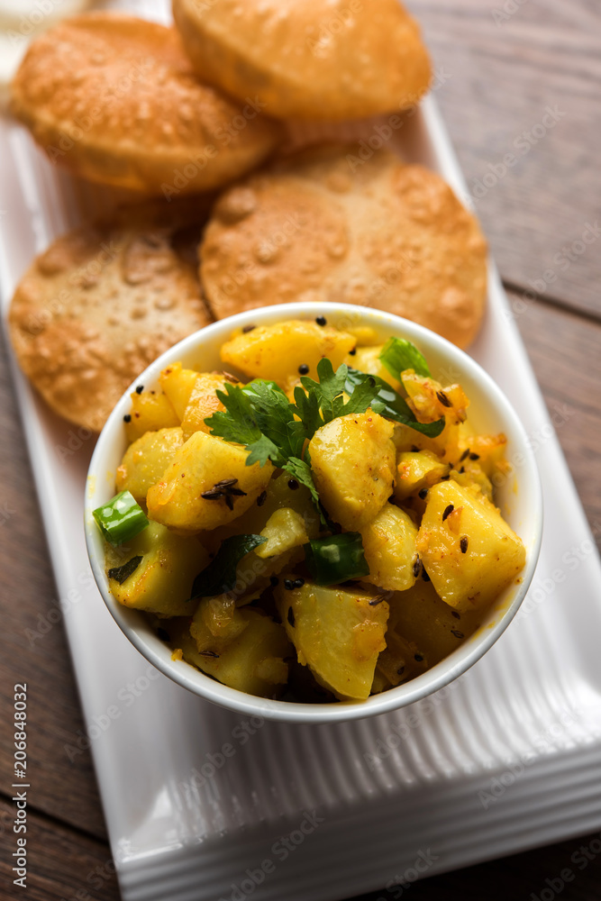 Chatpate Masala Aloo Sabzi fry OR Bombay potatoes served with fried puri or Indian bread made up of wheat in a plate, selective focus Chatpate Masala Aloo Sabzi fry OR Bombay potatoes served with fried puri or Indian bread made up of wheat in a plate, selective focus