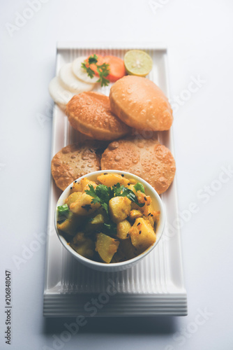 Chatpate Masala Aloo Sabzi fry OR Bombay potatoes served with fried puri or Indian bread made up of wheat in a plate, selective focus photo