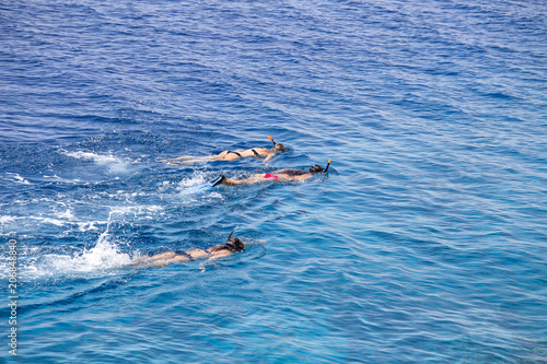 Three young girls snorkeling in blue waters above coral reef on red sea in Sharm El Sheikh, Egypt. People and lifestyle concept.
