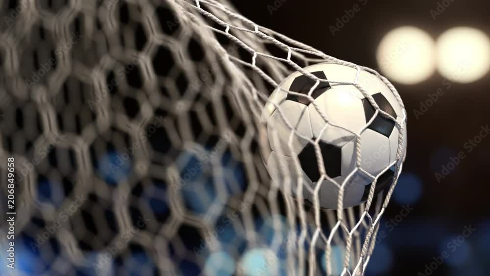 Soccer ball flies into the net on a stadium with yellow and blue lights. The movement at the beginning is accelerated then slowly