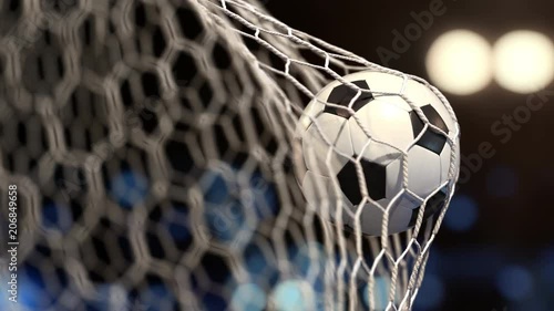 Soccer ball flies into the net on a stadium with yellow and blue lights. The movement at the beginning is accelerated then slowly photo
