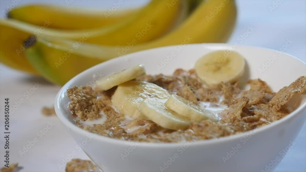 Corn flakes with milk are in a bowl. pieces of banana fall on the top of this delicious breakfast. Close-up shot Corn flakes with milk are in a bowl. pieces of banana fall on the top of this delicious breakfast. Close-up shot