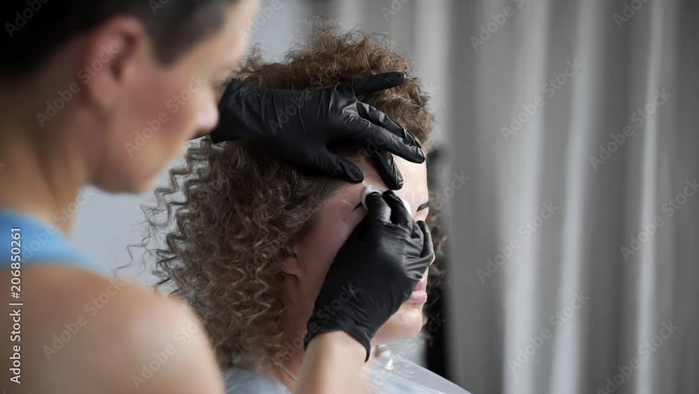 Stylist wipes eyebrows with a sponge after eyebrow coloring at the beauty salon, eyebrow coloring and correction, coloring by henna, beauty and healthcare, cosmetic services Stylist wipes eyebrows with a sponge after eyebrow coloring at the beauty salon, eyebrow coloring and correction, coloring by henna, beauty and healthcare, cosmetic services