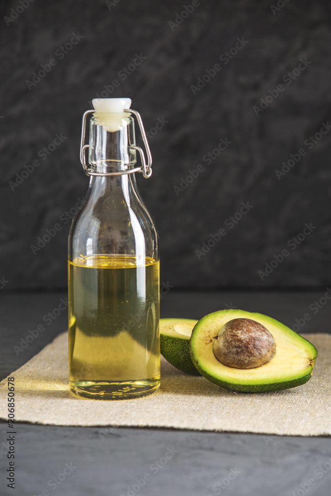 Avocado fruit and oil in glass bottle on dark background. Concept organic eco products for food and cosmetic procedures Avocado fruit and oil in glass bottle on dark background. Concept organic eco products for food and cosmetic procedures