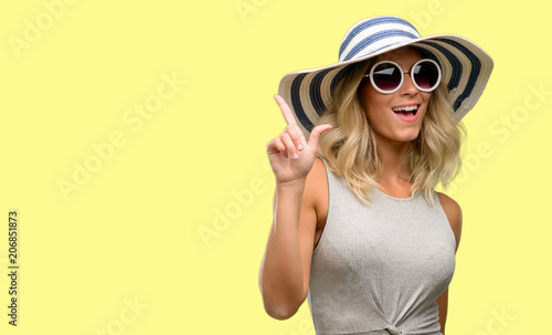 Young woman wearing sunglasses and summer hat pointing away side with finger