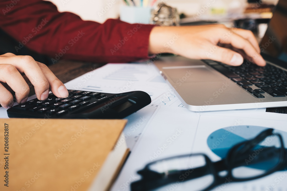 Close up of businessman or accountant hand holding pencil working on calculator to calculate financial data report, accountancy document and laptop computer at office Close up of businessman or accountant hand holding pencil working on calculator to calculate financial data report, accountancy document and laptop computer at office