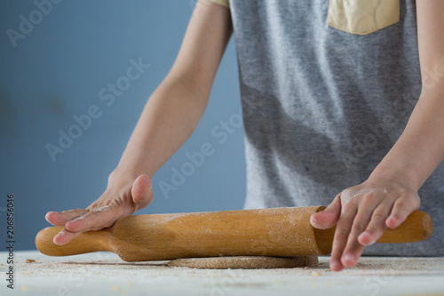 child hands rolling out dough for pizza, on a wooden table with flour