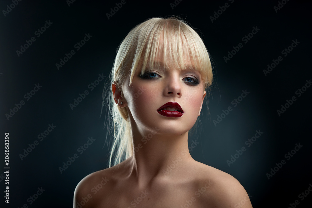Horizontal frontview of model wearing evening make up. Girl having big blue  eyes, short blonde hair and pretty face with plump lips, covered with dark red  lipstick. Posing with opened shoulders. Stock