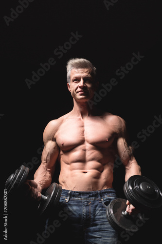 Handsome power athletic man with dumbbell confidently looking forward. Strong bodybuilder with six pack, perfect abs, shoulders, biceps, triceps and chest. Strength and motivation