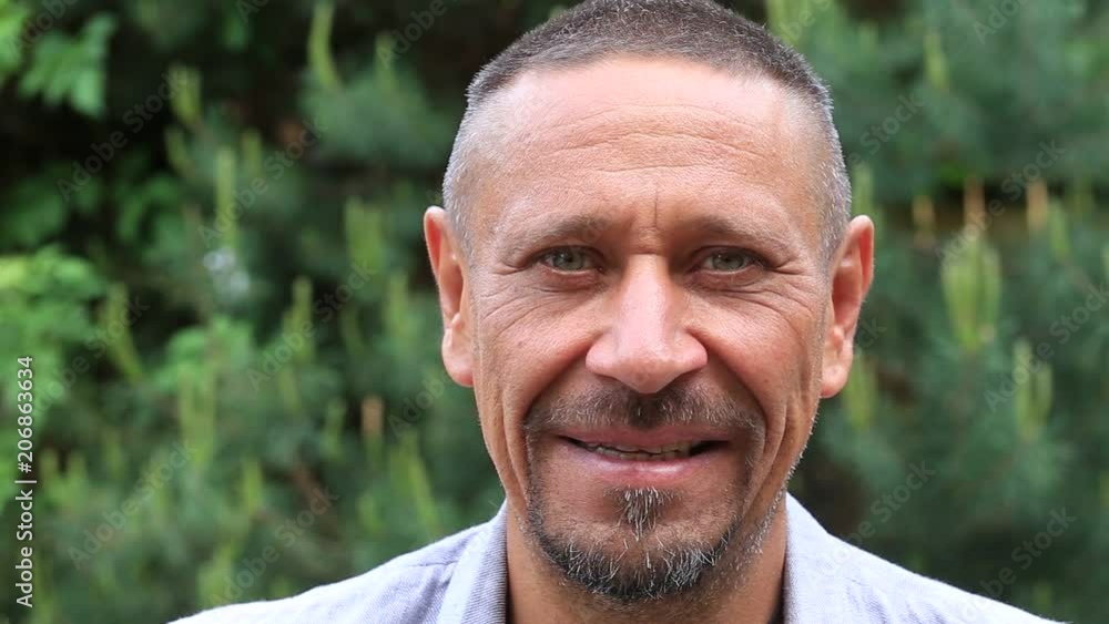 People and lifestyle concept. Happy middle-aged unshaven man with cheerful smile outdoor against green nature background. Adult man portrait close up People and lifestyle concept. Happy middle-aged unshaven man with cheerful smile outdoor against green nature background. Adult man portrait close up