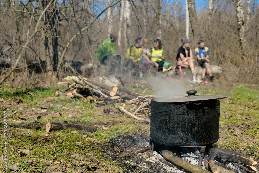 Group of friends sitting on grass while soup cooking on fire Group of friends sitting on grass while soup cooking on fire