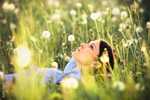 Summer scene. Girl in white dandelions enjoying evening time. Young woman relaxing outdoors.