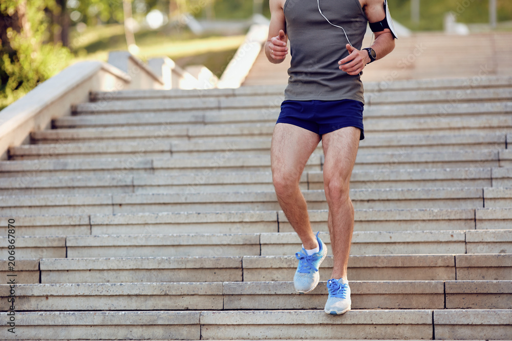A young male runner runs down the steps in the park in the summer. A young male runner runs down the steps in the park in the summer.