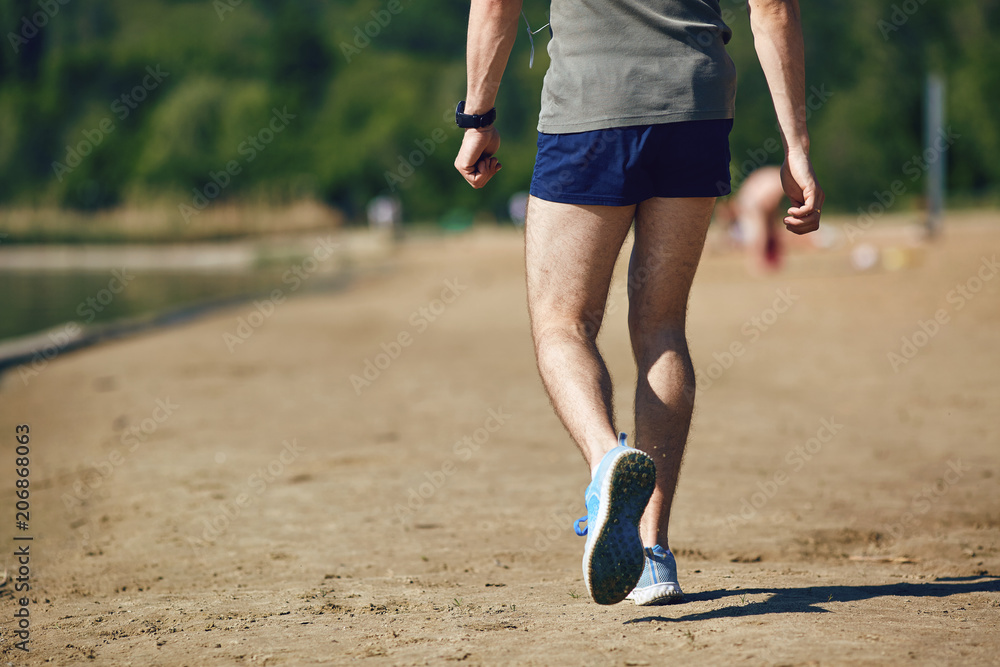 A male runner walks after training in the park in the summer.