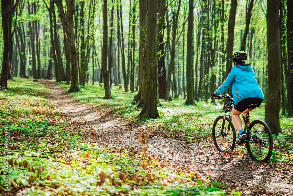 Naklejka premium young woman ride bicycle in forest by trail