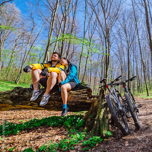 couple sit on stump resting after cycling by forest