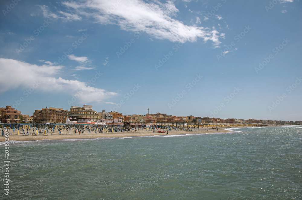 Overview of the beach and town of Ostia between the Mediterranean sea and sunny sky. The town is a seaside resort and ancient port of Rome. Located in the Lazio region