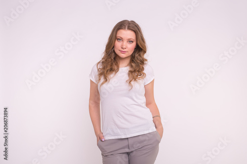Young woman standing with hands in pockets, wearing white tshirt with copy space for your logo or text, isolated on white background © satura_