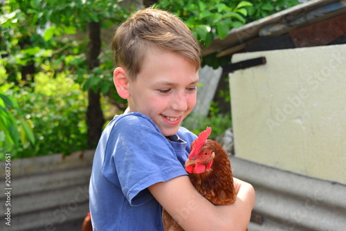 A boy is holding a brown chicken and smiling