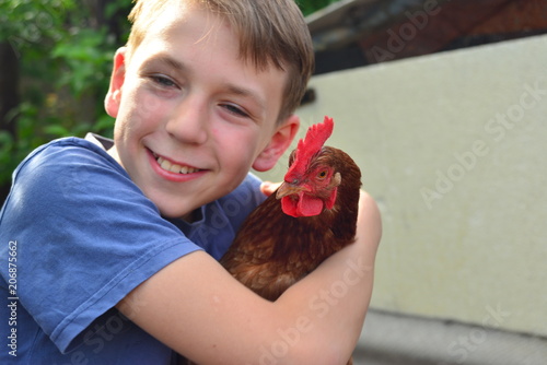 A boy holds a brown chicken in his hand and smiles and kisses her and hugs him. photo