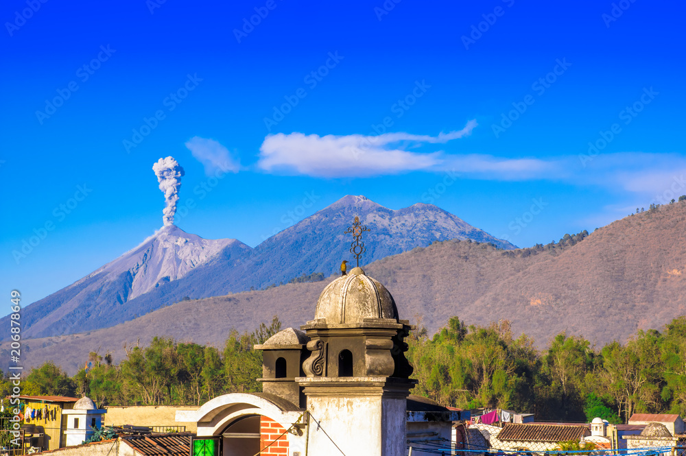 Beautiful landscape of huge mountain in process of aruption with a column of ash, view from the rooftops of the building in Antigua city in gorgeous sunny day and blue sky