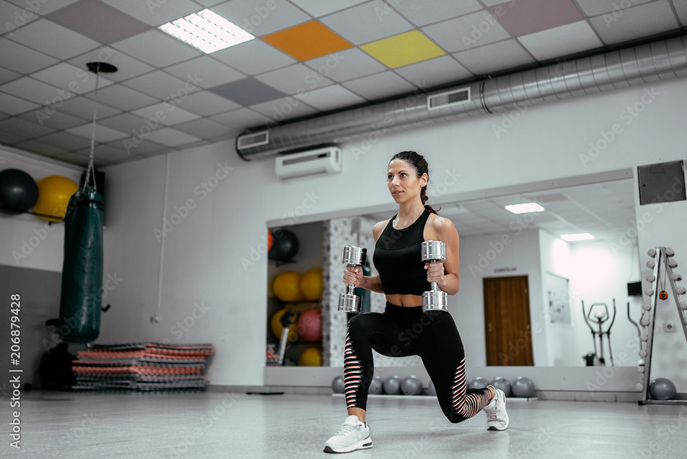 Obraz premium Young beautiful woman working out with dumbbells in the gym.