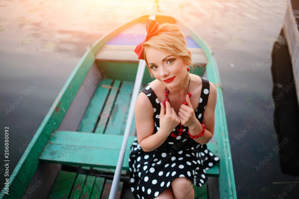 Beautiful young woman dressed dressed in a boat on a lake shore