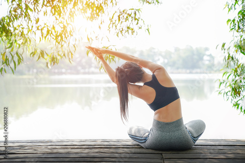 Fototapeta Naklejka Na Ścianę i Meble -  Young woman doing yoga in morning park near lake