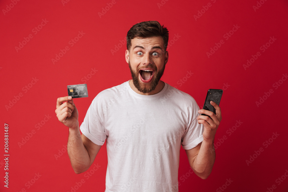 Excited screaming young man holding mobile phone and credit card. Looking camera. Excited screaming young man holding mobile phone and credit card. Looking camera.