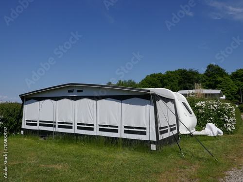 Wohnwagen auf einem deutschen Campingplatz mit einem wetterfesten Zelt davor. Die Fenster sind geschlossen.