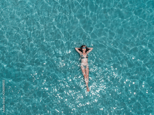 Beautiful young woman floating in crystal clear water, aerial shot