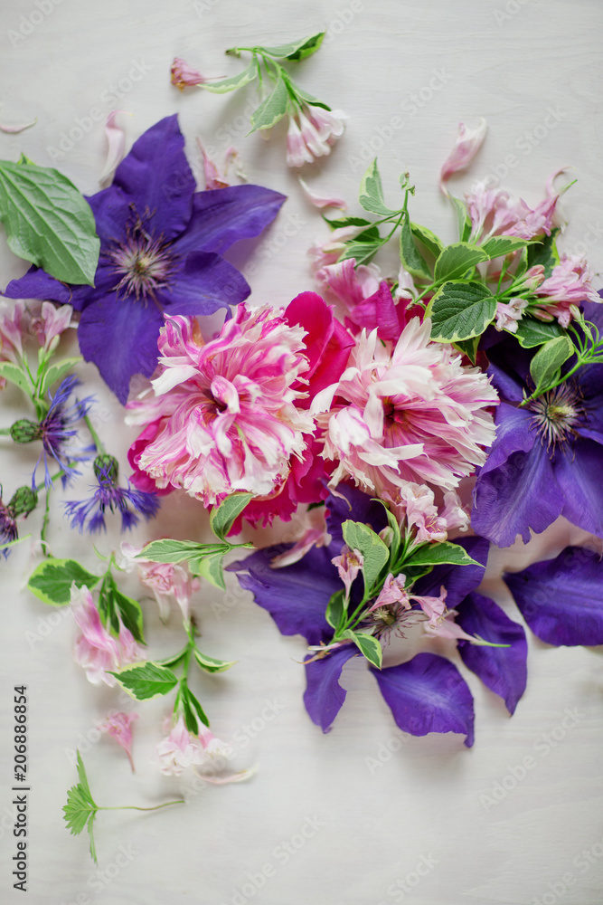 Beautiful pink, rose peonies and violett purple clematis flowers on white wood plate, can be used as background